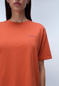 Short-sleeve, crew-neck t-shirt in bright orange, made of cotton blend, featuring a small purple logo on the left chest area.