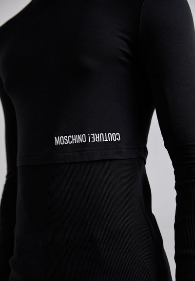 Must mustärga pika varrukaga särk, mis on valmistatud siledast kangast, alumises osas ribakujundusega ja millel on valge silmkoelise kirja "Moschino Couture!".