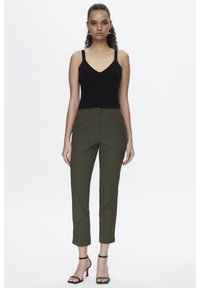 Zwarte getailleerde tanktop met dunne bandjes, gecombineerd met groene geruite broeken. De broeken hebben een cropped snit en voorzakken. Zwarte sandalen met bandjes.
