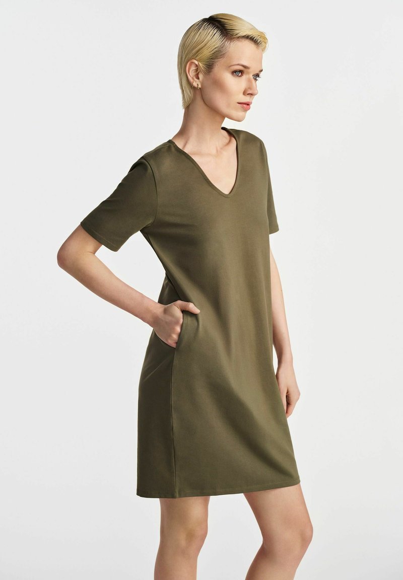 Oliwkowa sukienka z dekoltem w kształcie litery V, krótkimi rękawami i bocznymi kieszeniami. Wykonana z gładkiego, matowego materiału, o luźnym kroju i długości do kolan.