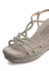 Beige wedge sandaal met gevlochten metallic banden en een gevoerd suède voetbed. De wedge is omwikkeld met geweven materiaal.