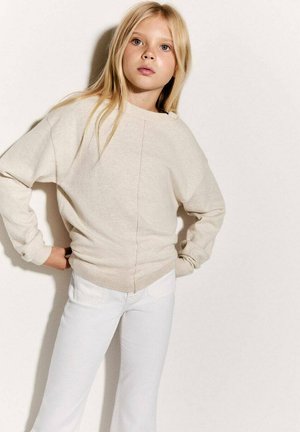 Maglione beige con una vestibilità comoda, maniche larghe e orlo a forma di V, abbinato a jeans bianchi con tasche frontali.