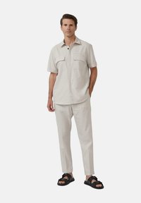 Chemise boutonnée à manches courtes gris clair avec deux poches poitrine, associée à un pantalon gris clair assorti et des sandales noires au design à lanières.