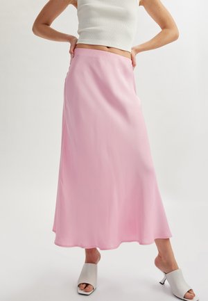 Pink satin maxi skirt with a flowy silhouette, smooth texture, and a subtle sheen. Paired with light gray open-toe mules.