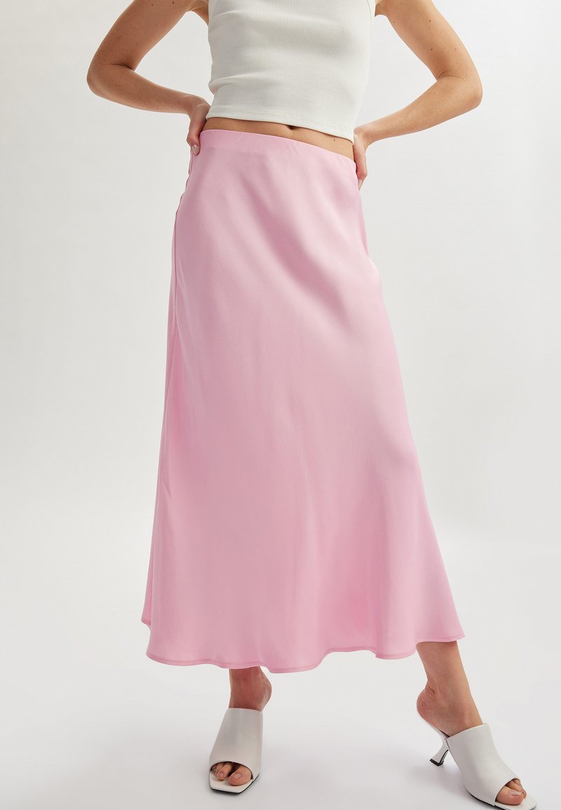 Jupe maxi en satin rose avec une silhouette fluide, une texture lisse et un éclat subtil. Associe à des mules ouvertes grises claires.