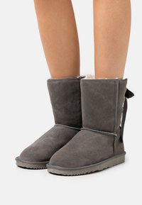 Bottes cheville grises en daim avec une doublure douce, dotées d'une semelle plate et d'un détail de couture. L'arrière est orné d'un ruban en tissu.