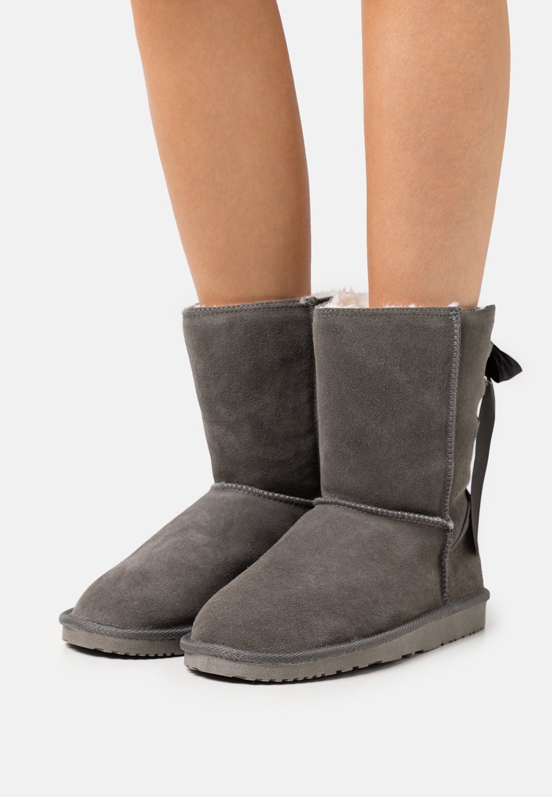 Bottes cheville grises en daim avec une doublure douce, dotées d'une semelle plate et d'un détail de couture. L'arrière est orné d'un ruban en tissu.