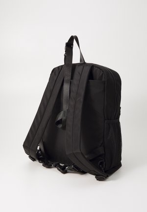 Schwarzer Stoff-Rucksack mit zwei gepolsterten Schultergurten, einem Reißverschluss-Hauptfach, seitlichen Mesh-Taschen und einer schlanken rechteckigen Form.