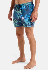 Męskie kąpielówki w kolorze niebieskim z tropikalnym wzorem liści. Posiadają elastyczny pasek w talii z troczkiem oraz małą naszywkę z logo z boku.