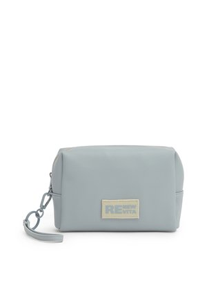 Bustina rettangolare azzurro chiaro con cerniera e cinturino da polso, con etichetta beige con testo parzialmente visibile.