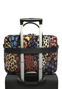 Eine lebendige, gemusterte Tasche für das Handgepäck mit einer Mischung aus Tiermotiven in Rot, Gelb und Blau, gesichert an einem schwarzen Rollkoffer mit silbernen Griffen.