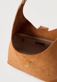 Καφέ δερμάτινη τσάντα με υφή, χρυσό κούμπωμα και αλυσίδα, ανοιχτή για να δείξει εσωτερική τσέπη σε μπεζ χρώμα με φερμουάρ.