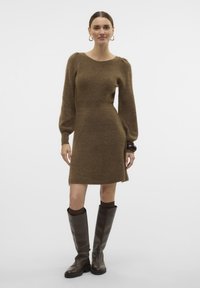 Abito in maglia marrone con lunghe maniche a sbuffo, corpino aderente e gonna svasata. Indossato con stivali alti in pelle marrone. Tessuto morbido.