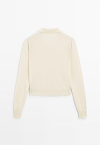 Pull court de couleur crème avec un col à revers, manches longues et poignets côtelés, fabriqué dans un matériau doux et texturé.