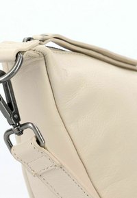 Bolso de cuero beige con una textura suave, que presenta un cierre metálico y detalles de costura. La forma es angular y cuenta con un cierre de cremallera en la parte superior.