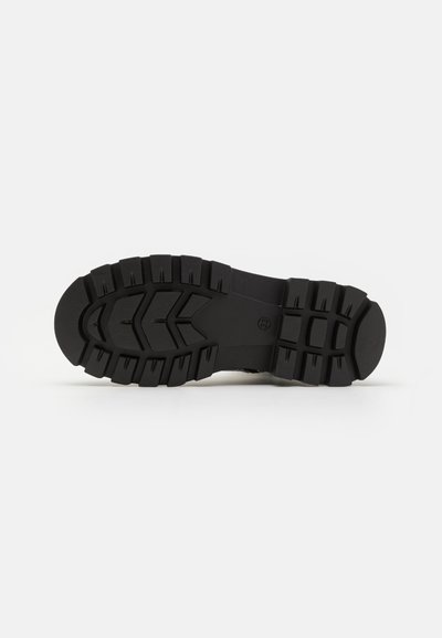 Semelle de chaussure en caoutchouc noir avec des sculptures profondes, présentant un design segmenté et une surface texturée pour l'adhérence. Les accents comprennent un panneau central lisse.