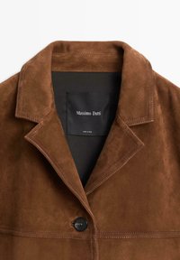 Bruine suède jas met een reverskraag, zwarte knoopsluiting en een onopvallend binnenlabel met "Massimo Dutti". Gladde textuur, getailleerd ontwerp.