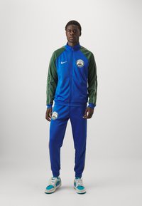 Tracksuit set in blue and green, featuring a full zip jacket with a logo and side stripes, paired with matching pants and sneakers.