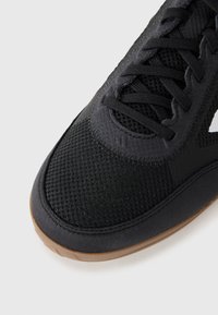 Black athletic shoe with mesh toe, suede accents, black laces, and gum rubber sole on a white background.