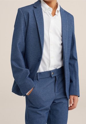 Niebieska marynarka w wzory z dopasowanymi spodniami, z klapą z wycięciem, subtelną teksturą oraz białą koszulą na guziki pod spodem.