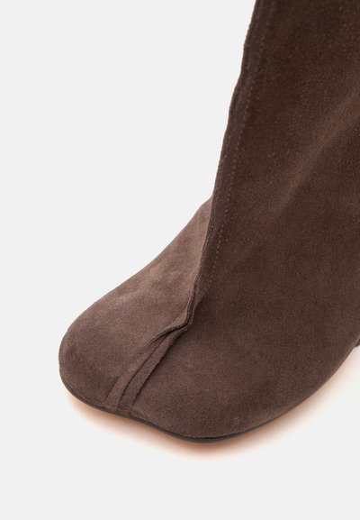 Botte en daim marron avec une couture cousue courant verticalement au centre devant et un bout carré arrondi.