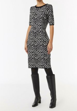 Woman wearing black and white zebra print knee-length dress with half sleeves, black tights, and black knee-high heeled boots.