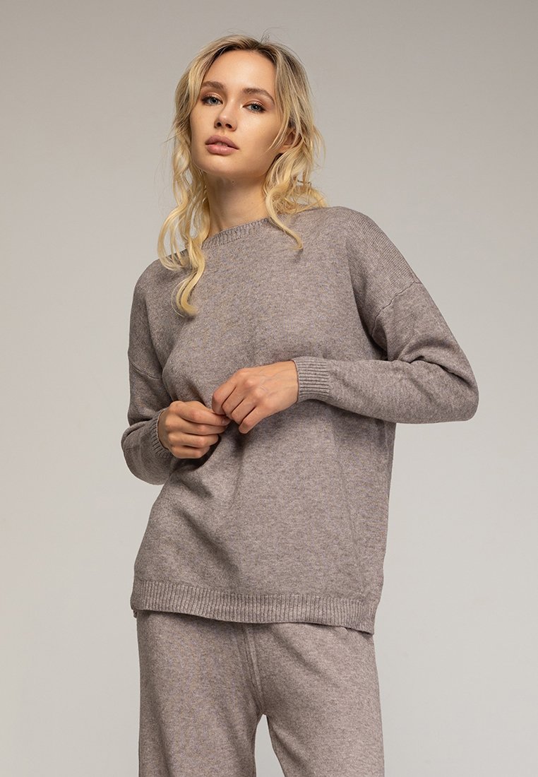 Suéter de punto gris claro con puños y dobladillo acanalados, que presenta un corte holgado y un escote redondeado. Textura suave y diseño casual.