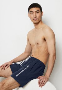 Marina badshorts med vit dragsko, med tryckt text på sidan. Tillverkad av ett lätt och snabbtorkande tyg med en avslappnad passform.