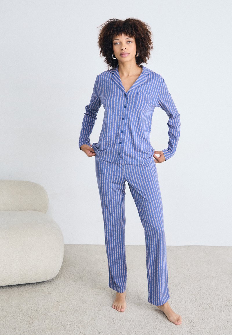 Blå och vit randig pyjamas med skjorta med knappar, lång ärm, bröstficka och matchande raka byxor. Mjuk tygtextur.
