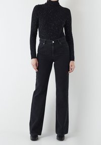 Czarny dopasowany sweter z golfem z metalicznymi zdobieniami, połączony z czarnymi spodniami z wysokim stanem i dzwonami. Gładka tekstura i klasyczny design.