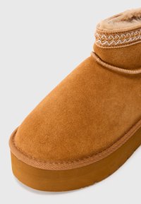 Stivaletto in camoscio marrone con cuciture decorative intorno al polsino e morbida fodera in pelliccia, dotato di una spessa suola in gomma.