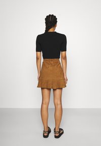 Haut noir à manches courtes associé à une mini-jupe en daim marron avec un ourlet à volants. Sandales noires ornées de ferrures décoratives complètent le look.