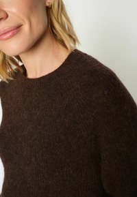 Hnědý, texturovaný svetr s kulatým výstřihem a dlouhými rukávy. Měkká, chlupatá tkanina s útulným vzhledem. Minimalistický design, bez vzorů.