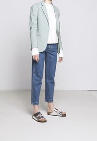 Jasnozielona kraciasta marynarka na białym swetrze, zestawiona z wysokim stanem niebieskimi dżinsami i srebrnymi sandałami z ciemnymi paskami.