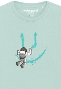 T-shirt bleu clair présentant un astronaute utilisant de la peinture en spray pour créer un graphique de smiley turquoise. Tissu doux avec un col rond.
