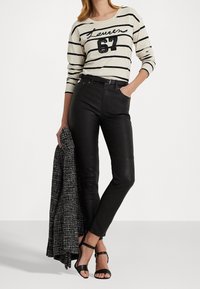 Svarta läderbyxor i kombination med en beige randig långärmad skjorta med "Lauren 67" i paljetter. Håller en svart texturerad jacka.