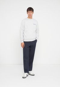 Sweatshirt gris avec des poignets et un ourlet côtelés, arborant un logo bleu. Associé à un pantalon bleu foncé et des baskets gris-blanc avec des rayures noires.