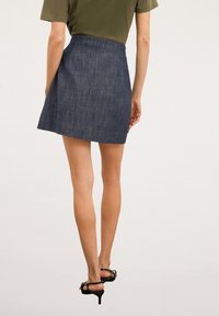 Jupe mini en denim à coupe droite, de couleur bleu foncé, avec une finition texturée subtile. Elle possède une ceinture basique et une longueur au-dessus du milieu de la cuisse.