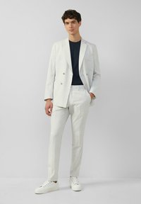 Jasnoszary, dwurzędowy garnitur o fakturowanym wykończeniu, w połączeniu z granatowym T-shirtem i białymi trampkami. Slim fit z dopasowanymi spodniami.