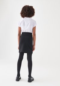 Blouse blanche à manches courtes, jupe noire, collants noirs et chaussures noires. La blouse présente des manches froncées ; la jupe a un design uni.