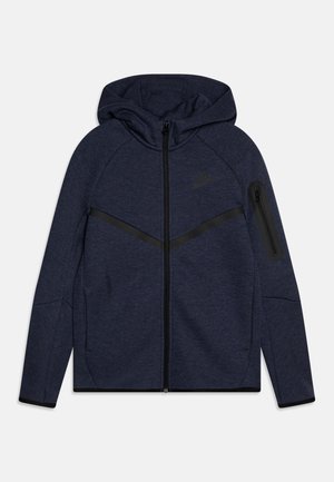 Dunkelblauer Hoodie mit durchgehendem Reißverschluss und angenähter Kapuze, schwarzen diagonalen Streifen, Reißverschlusstasche am linken Ärmel und dezentem Logo auf der Brust.