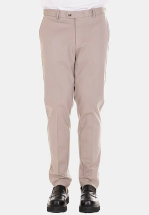 Pantaloni beige con design aderente, texture liscia e tasche laterali, abbinati a scarpe nere per contrasto.