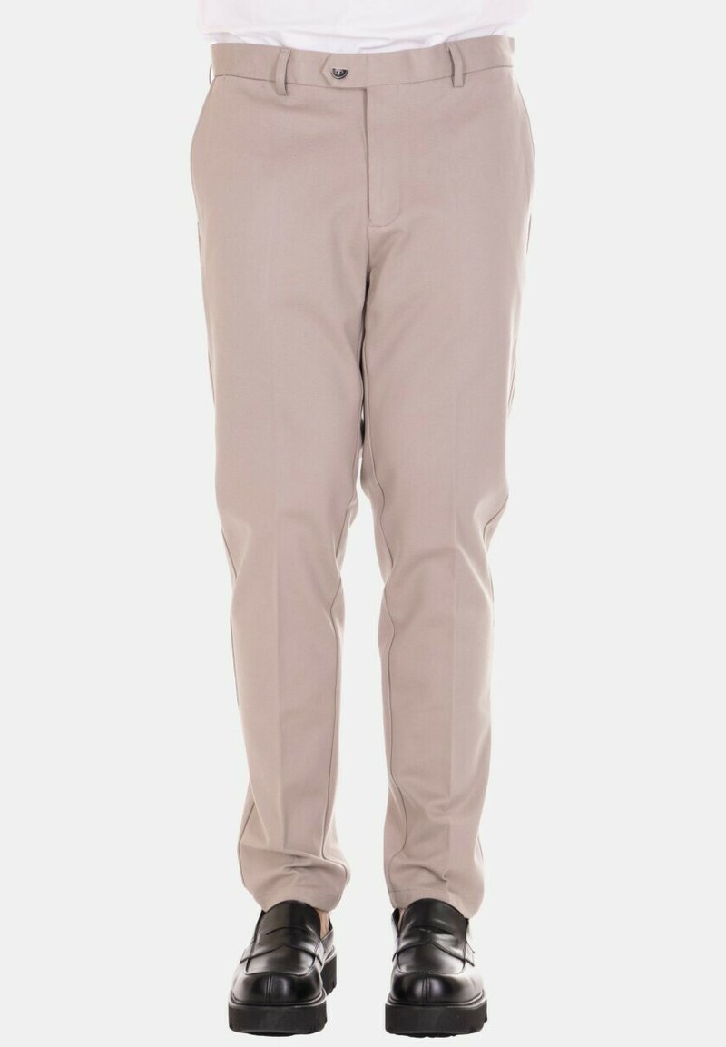 Pantaloni beige con design aderente, texture liscia e tasche laterali, abbinati a scarpe nere per contrasto.