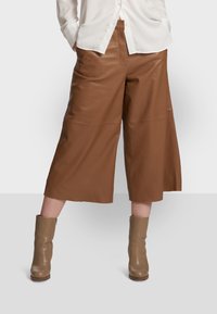 Brązowe skórzane kuloty z szerokimi nogawkami, charakteryzujące się gładką teksturą i kieszenią z przodu, zestawione z beżowymi botkami na obcasie.