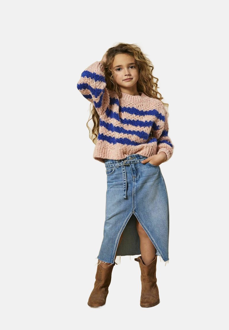 Stickad rosa tröja med blå ränder, ihop med en högmidjad denimbakelse med en framklippning och bruna ankelstövlar.