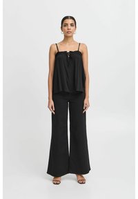 Top negru, fără mâneci, cu un decolteu plisat și detalii cu fundă, asortat cu pantaloni evazați negri. Textură uniformă a materialului, design minimalist.