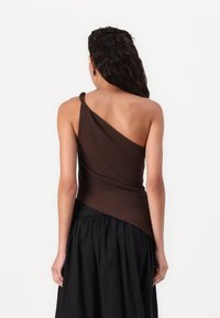 Top maro cu un umăr, cu țesătură drapată, prezentând un detaliu strâns la talie, asortat cu o fustă neagră. Textură netedă, design minimalist.