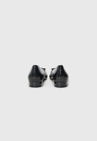 Mocassins noirs texturés avec une finition en motif serpent, petit talon, bout rond et un petit détail de nœud décoratif sur le dessus.
