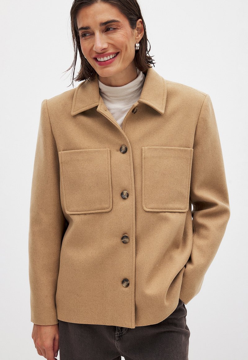 Beige wolblend jasje met een kraaghals, twee grote opgestikte zakken en knoopsluiting, met een gladde textuur en een gestructureerde pasvorm.