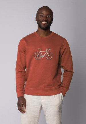 Rustfarbener Pullover aus weichem Stoff, mit einem weißen Fahrrad-Graphic auf der Vorderseite. Lange Ärmel mit Rippenbündchen und Saum.